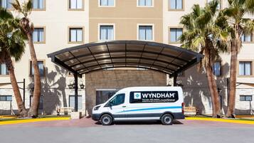 A Wyndham hotel with a covered entrance, palm trees, and a van parked in front.