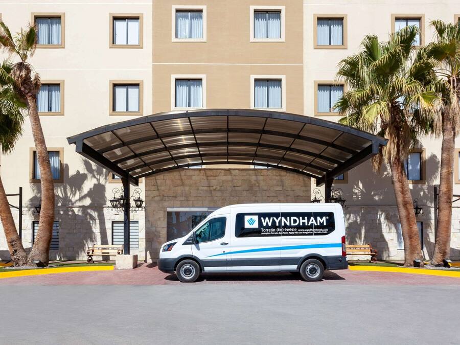 A Wyndham hotel with a covered entrance, palm trees, and a van parked in front.