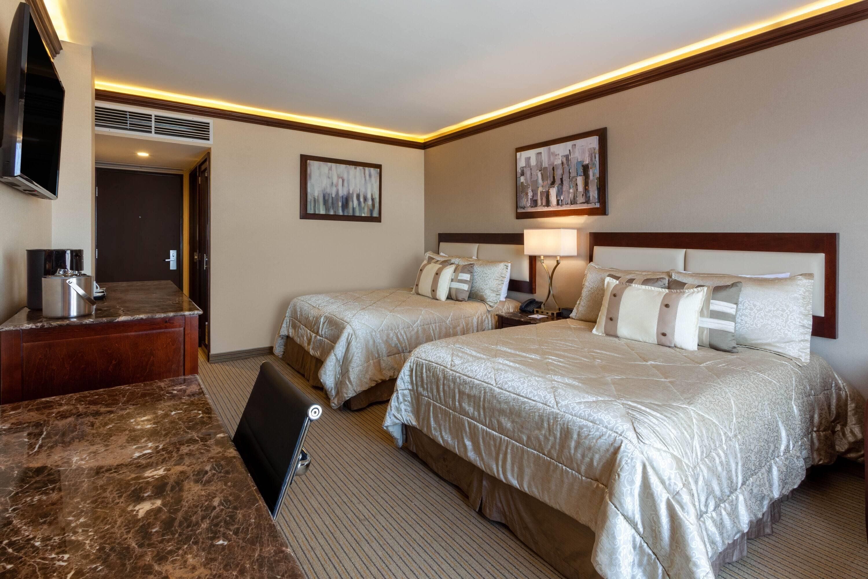 A hotel room with two beds, a desk, a TV, and artwork on the walls.