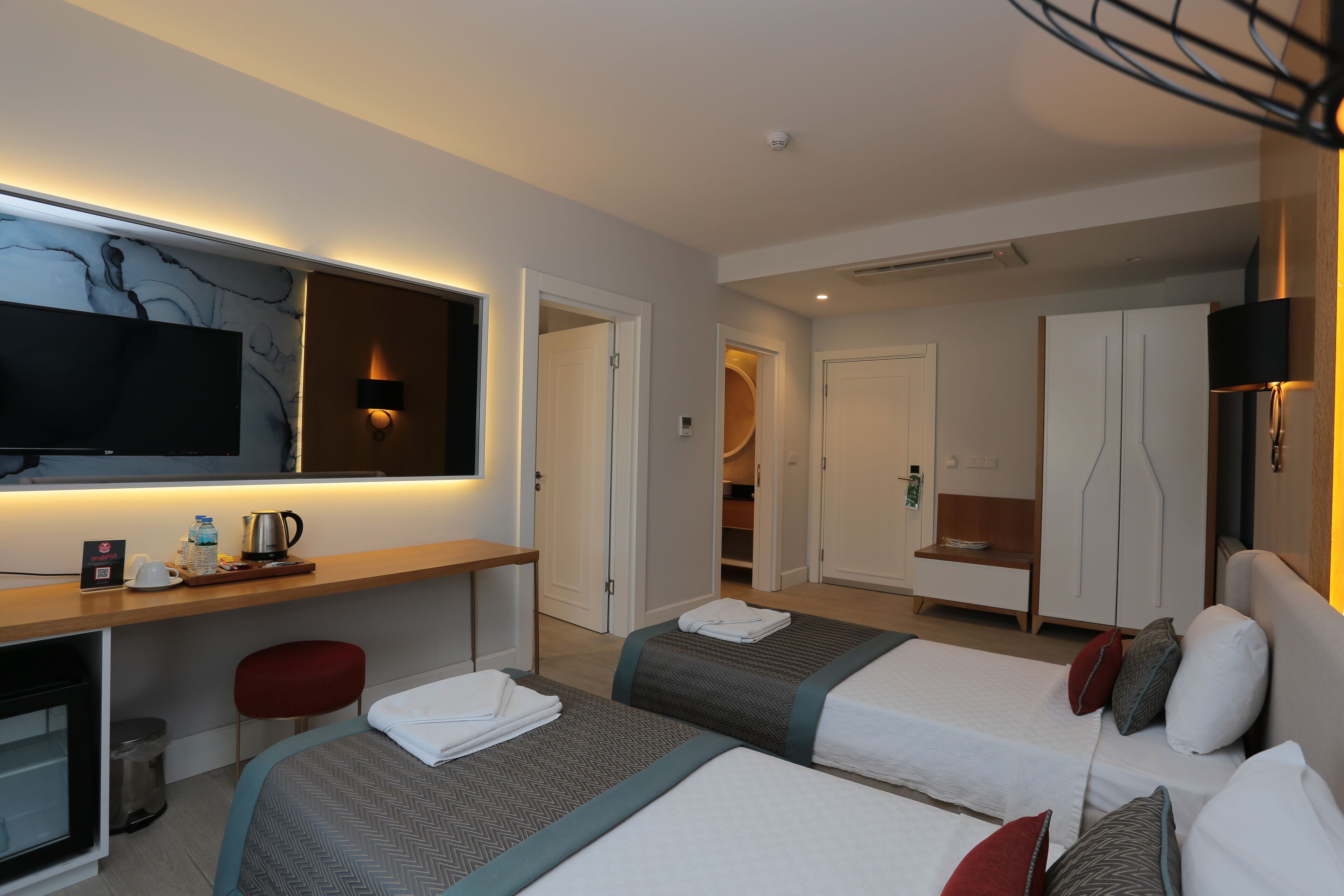 Ein Hotelzimmer mit zwei Betten, einem Schreibtisch, einem Flachbildfernseher, einer Minibar und einem Kleiderschrank.