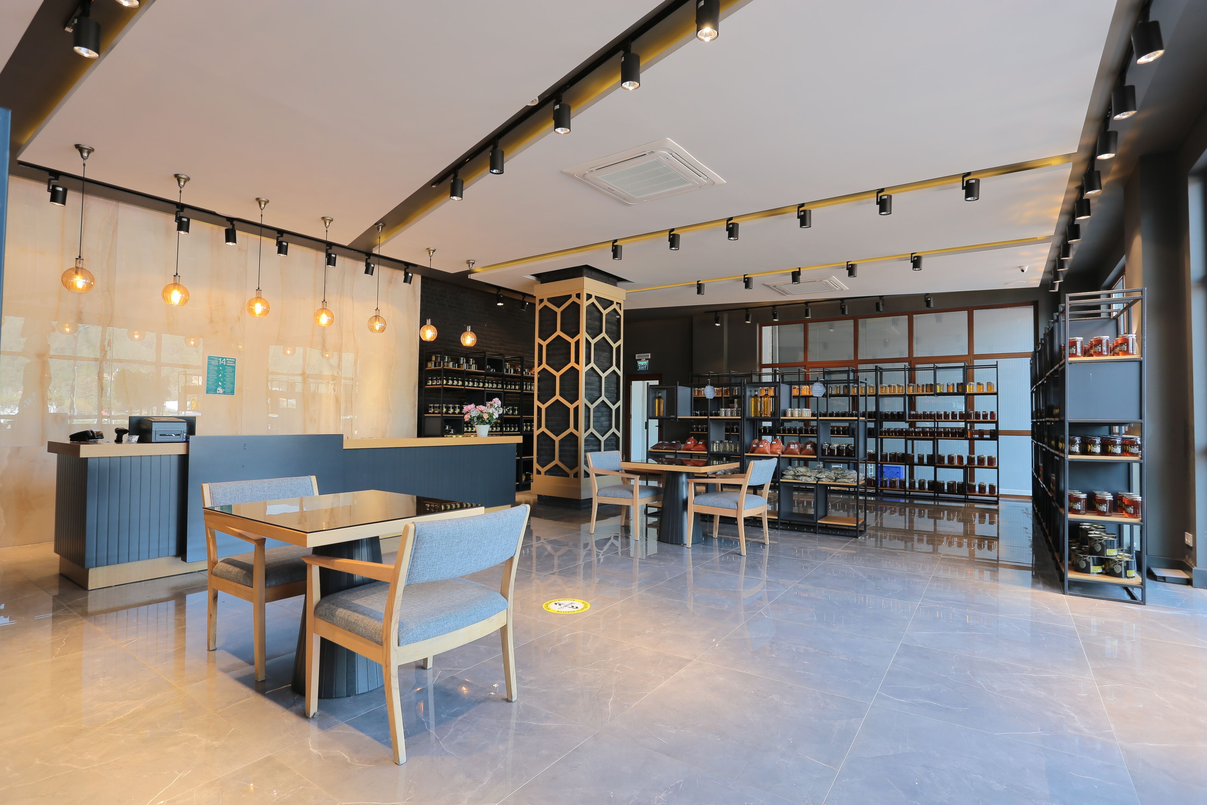 A modern cafe with a counter, seating area, and shelves stocked with jars.