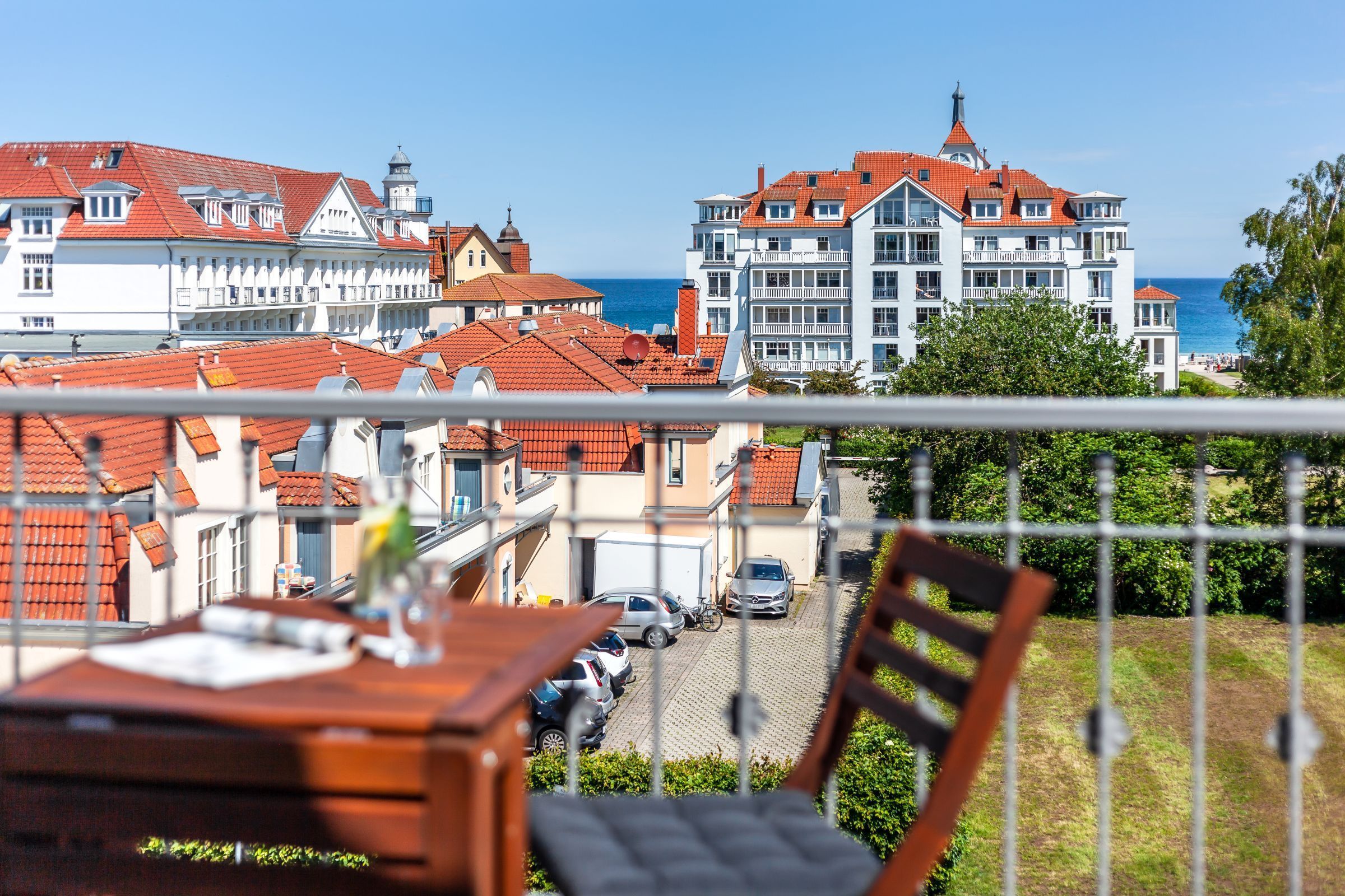 Un balcó amb vista a una població costanera, on es veuen edificis tradicionals amb teulades vermelles i un gran hotel amb una torre.