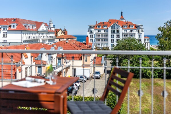 A balcony with a view of a coastal town, featuring traditional buildings with red roofs and a large hotel with a tower.