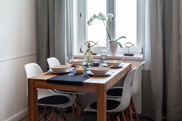 Une table à manger, avec des chaises blanches, une bouteille, des verres et une bougie.
