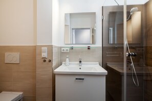 Un baño moderno con un lavamanos blanco, un espejo encima y una zona de ducha a la derecha.