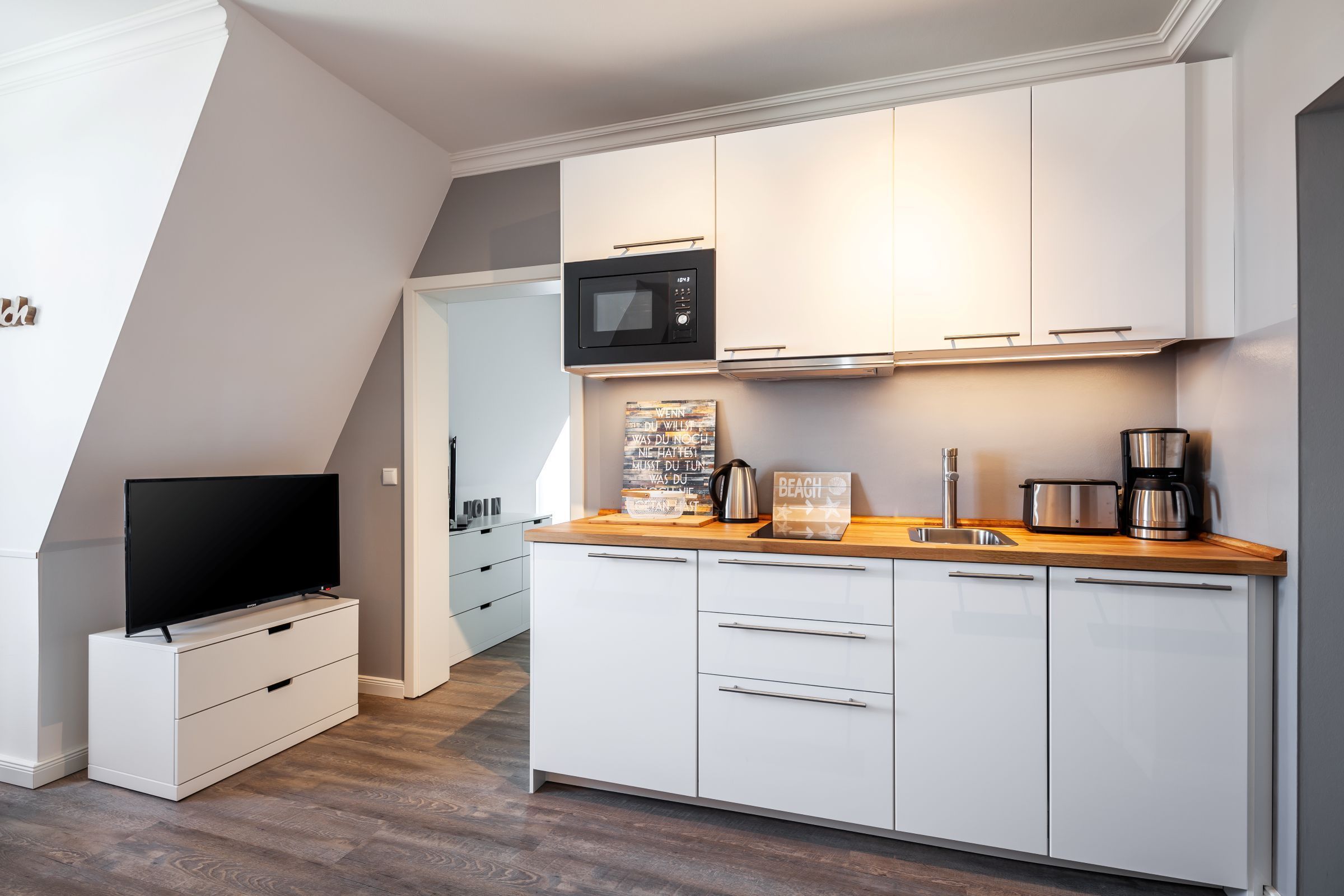 Eine moderne Küche mit weißen Schränken, einer Mikrowelle, einer Kaffeemaschine und einem Toaster.