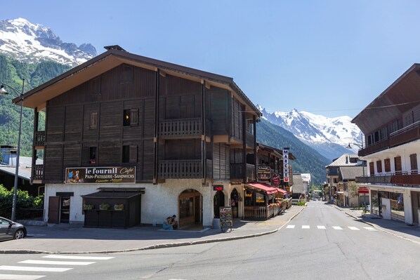 A wooden building with a café sign, a street with crosswalks, and snow-capped mountains in the background.