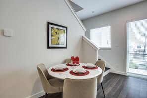 A dining area with a round table set for four, a framed abstract painting, and a staircase leading to an upper level.