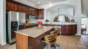 A modern kitchen with wooden cabinets, stainless steel appliances, and a central island with bar stools. - Beautifully furnished TownHome at shops (Plano)