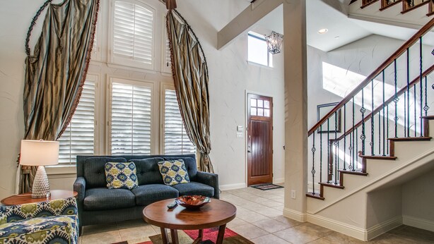 A spacious living room with a sofa, coffee table, and patterned rug. A staircase with wooden railings leads to an upper floor. - Beautifully furnished TownHome at shops (Plano)