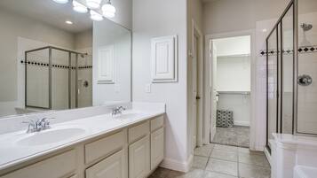 A modern bathroom with a large mirror, dual sinks, and a glass-enclosed shower area.