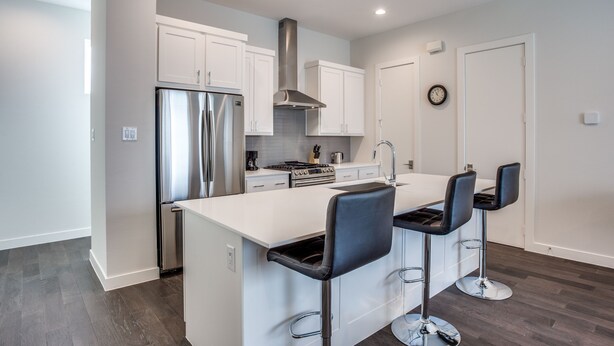 A modern kitchen with white cabinets, stainless steel appliances, and a central island with bar stools. - Upscale 2 bedroom Dallas TownHome (Dallas)