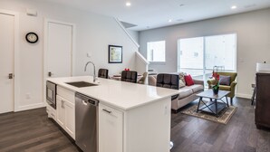 A modern kitchen with a dishwasher, a sink, and a dining area with a table and chairs. There is a sofa and a window with blinds in the living area. - Upscale 2 bedroom Dallas TownHome (Dallas)