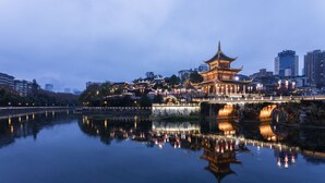 A traditional building with a multi-tiered roof, situated by a calm body of water reflecting lights, with modern buildings in the background. - Holiday Inn Guiyang City Center by IHG (Guiyang)