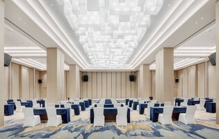 A conference room with rows of tables and chairs, a patterned carpet, and a modern ceiling design.