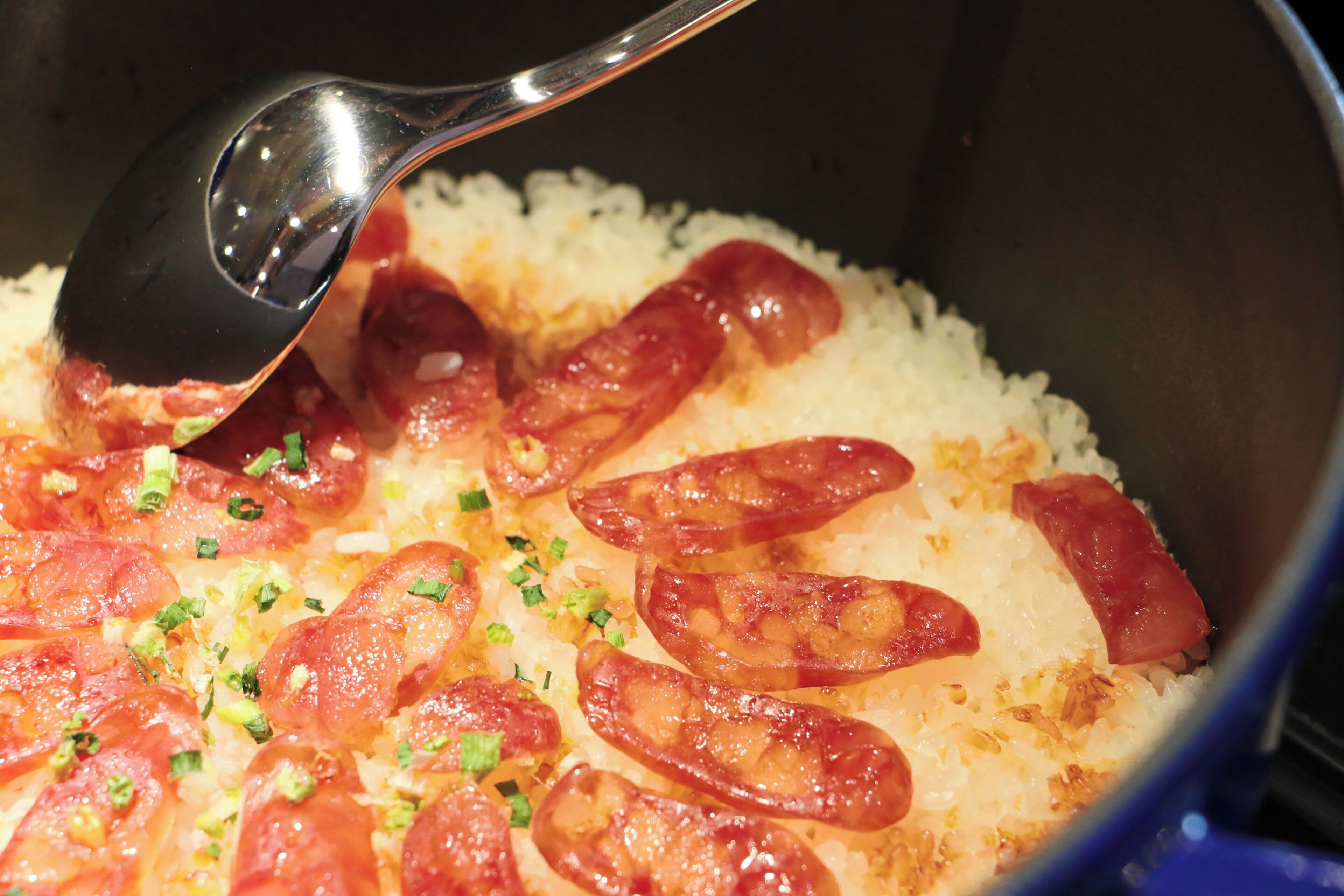 Primer plano de una olla con arroz, rodajas de tomate y cebollas verdes.