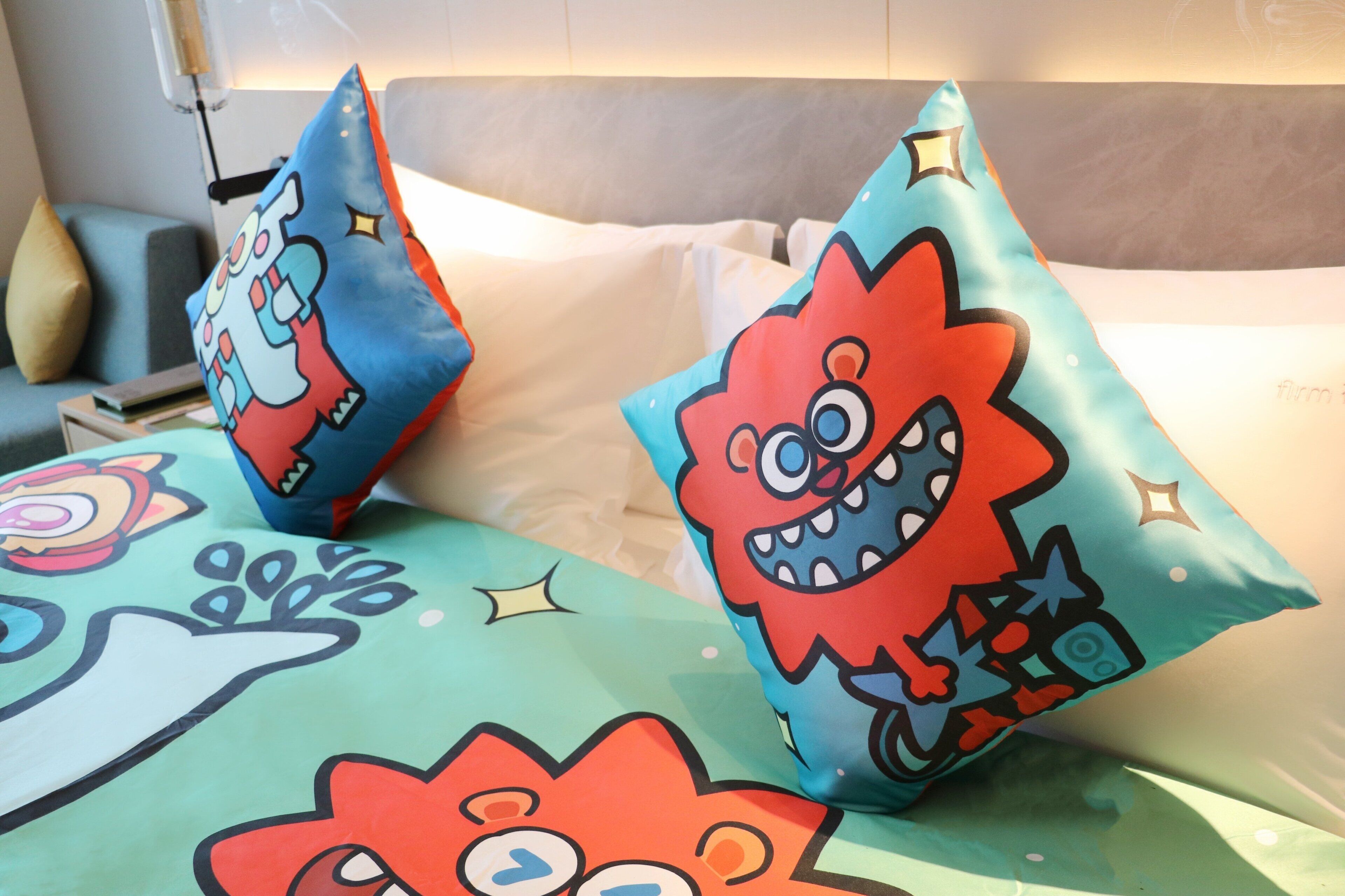 A bed with colorful, cartoon-themed pillows and a plain white pillow.