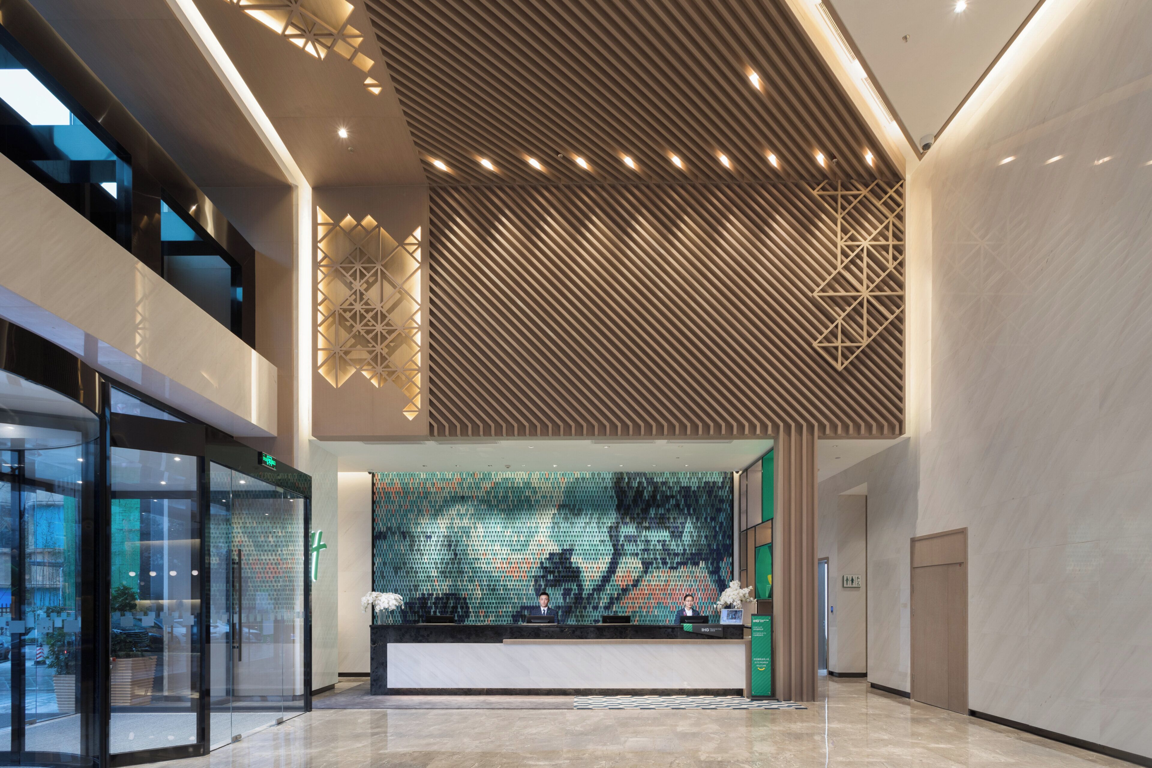 A modern reception area with a geometric patterned wall, a reception desk, and a glass entrance.