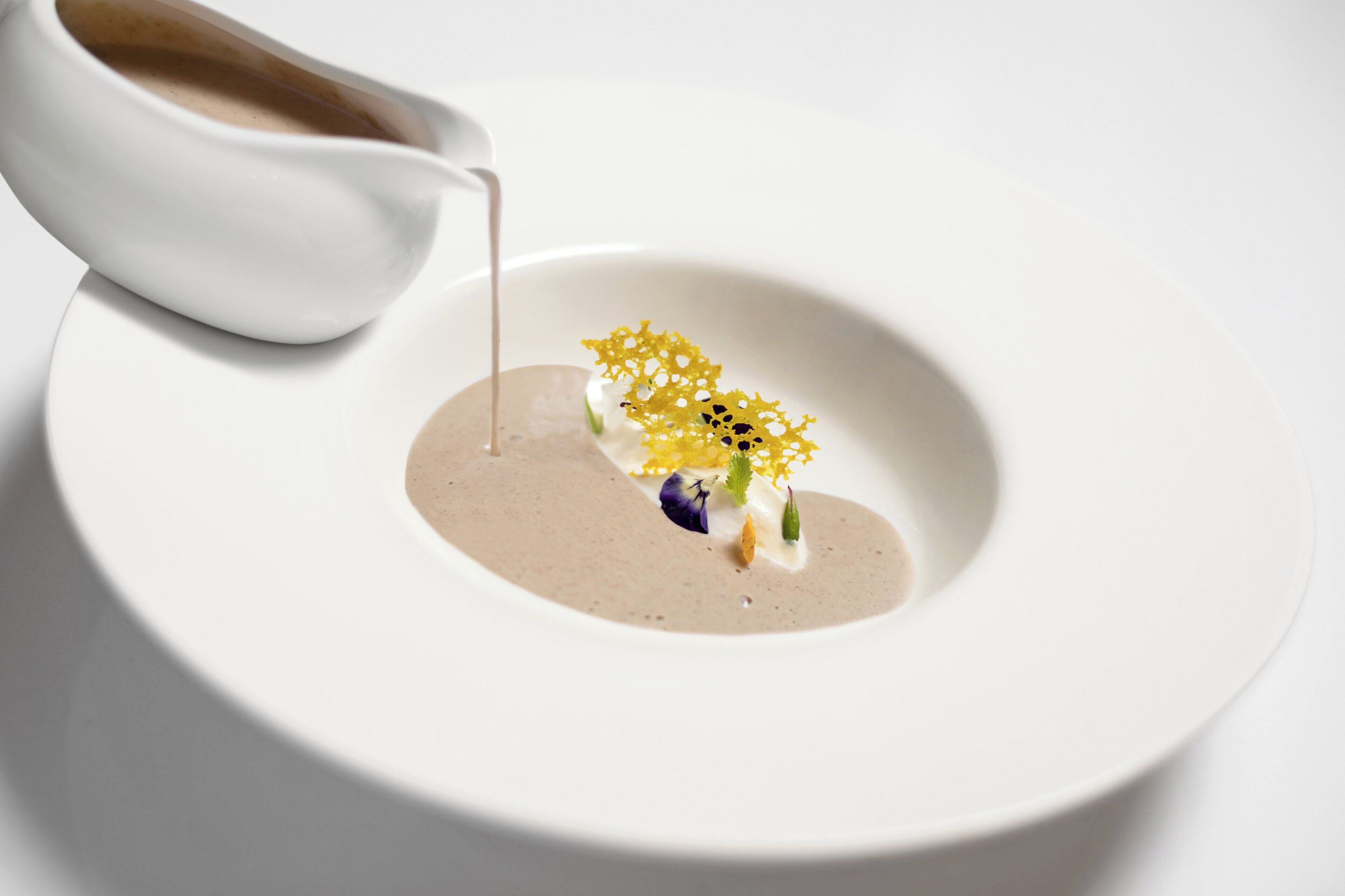 A white plate with a dessert consisting of a creamy substance, a yellow decorative element, and a small green item.