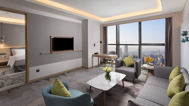 A modern hotel room with a large window, a flat-screen TV, a sofa, a coffee table, and a desk. - Holiday Inn Guiyang City Center by IHG (Guiyang)