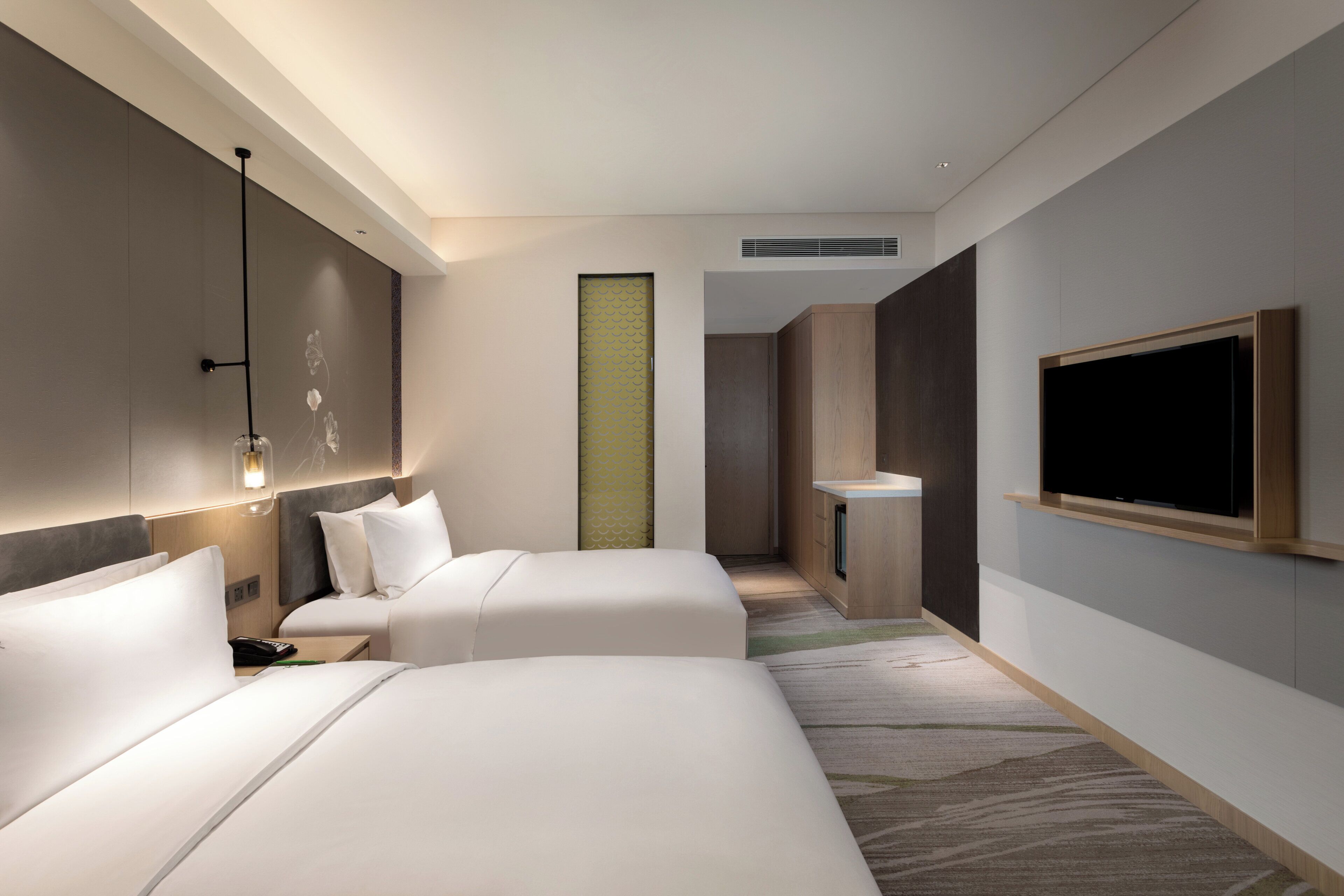 Camera d'albergo con due letti, una TV a schermo piatto, un comodino e un lampadario a parete.