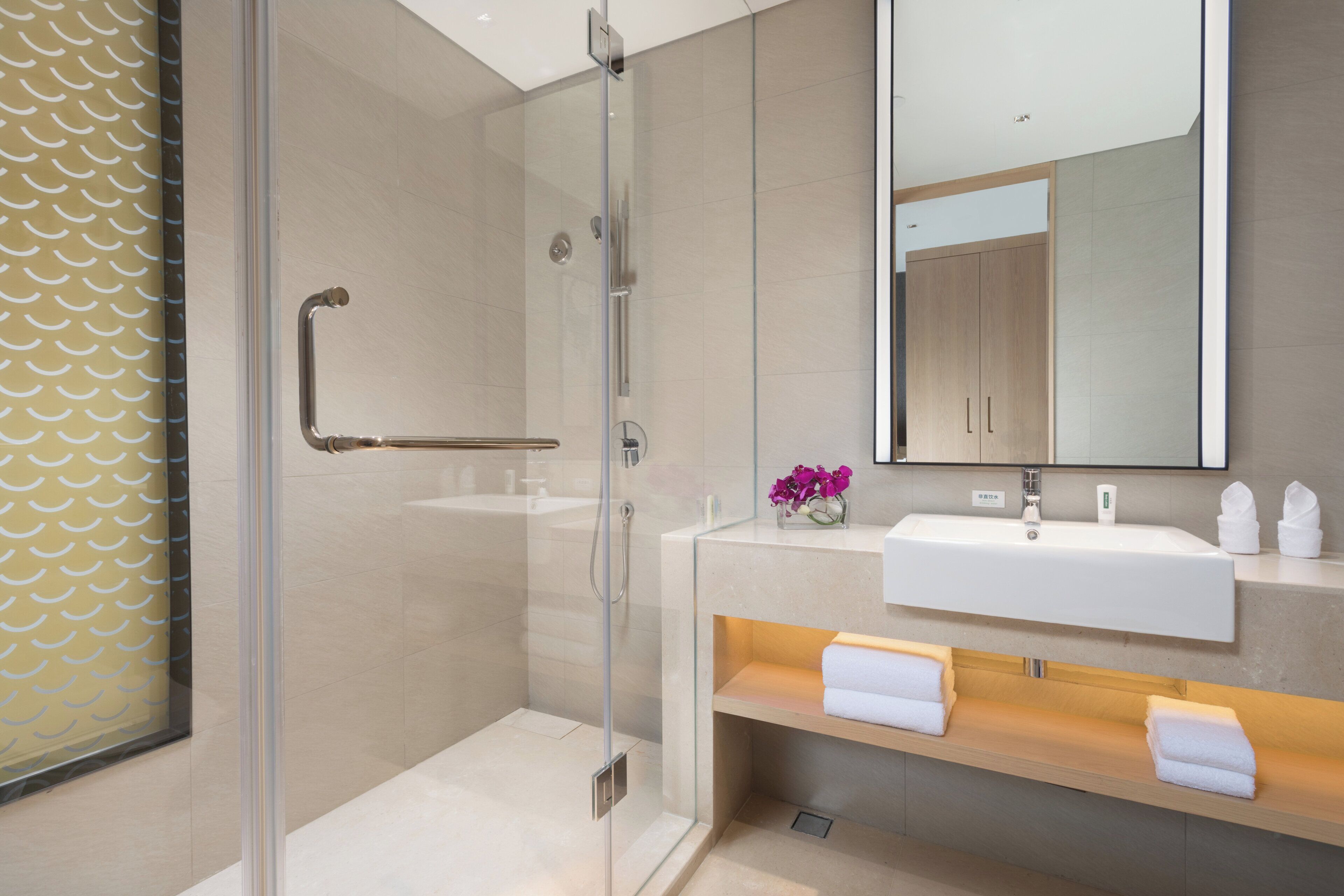 A modern bathroom with a glass shower enclosure, a white sink, and a mirror above it.