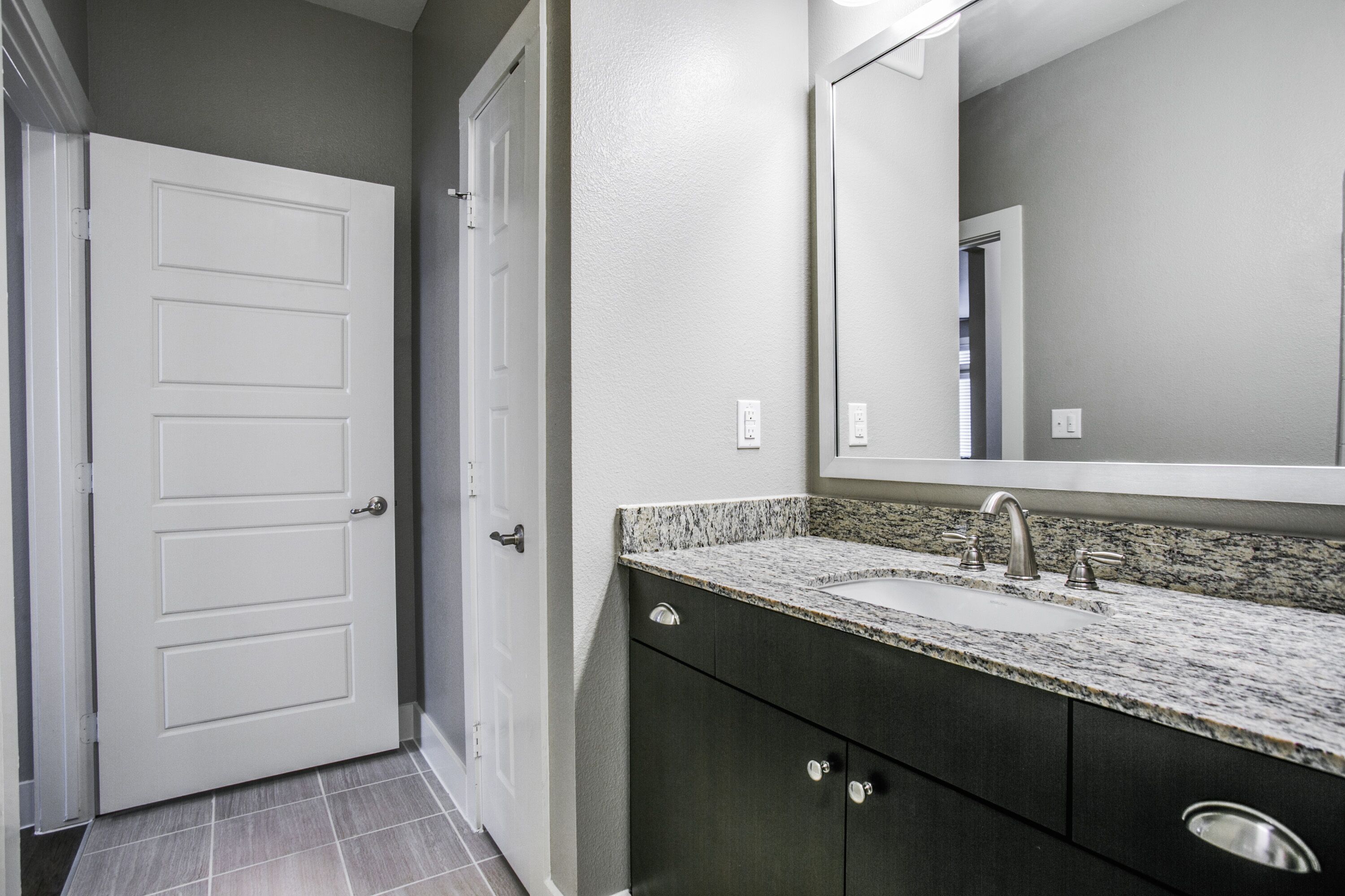 A bathroom with a white door, a granite countertop, a sink with a faucet, and dark cabinets.