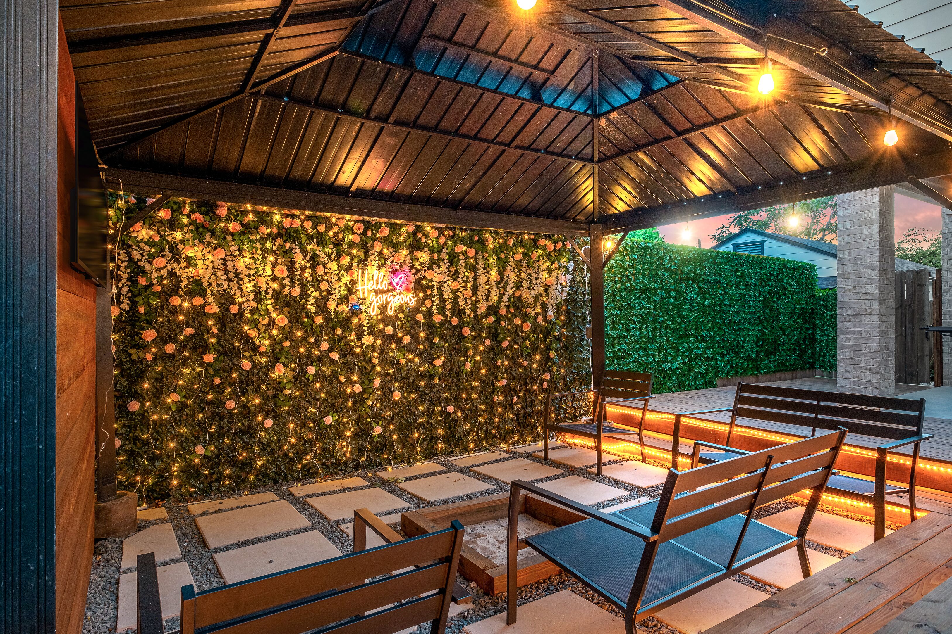 Une terrasse extérieure avec des bancs en bois et un mur décoré de fleurs et de guirlandes lumineuses.