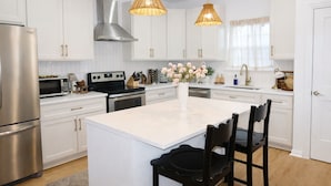 Une cuisine moderne avec des meubles blancs, des appareils en acier inoxydable, un îlot central et deux suspensions en osier.