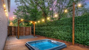 Une terrasse en bois avec un jacuzzi, entourée d’une clôture en bois et d’une haie.