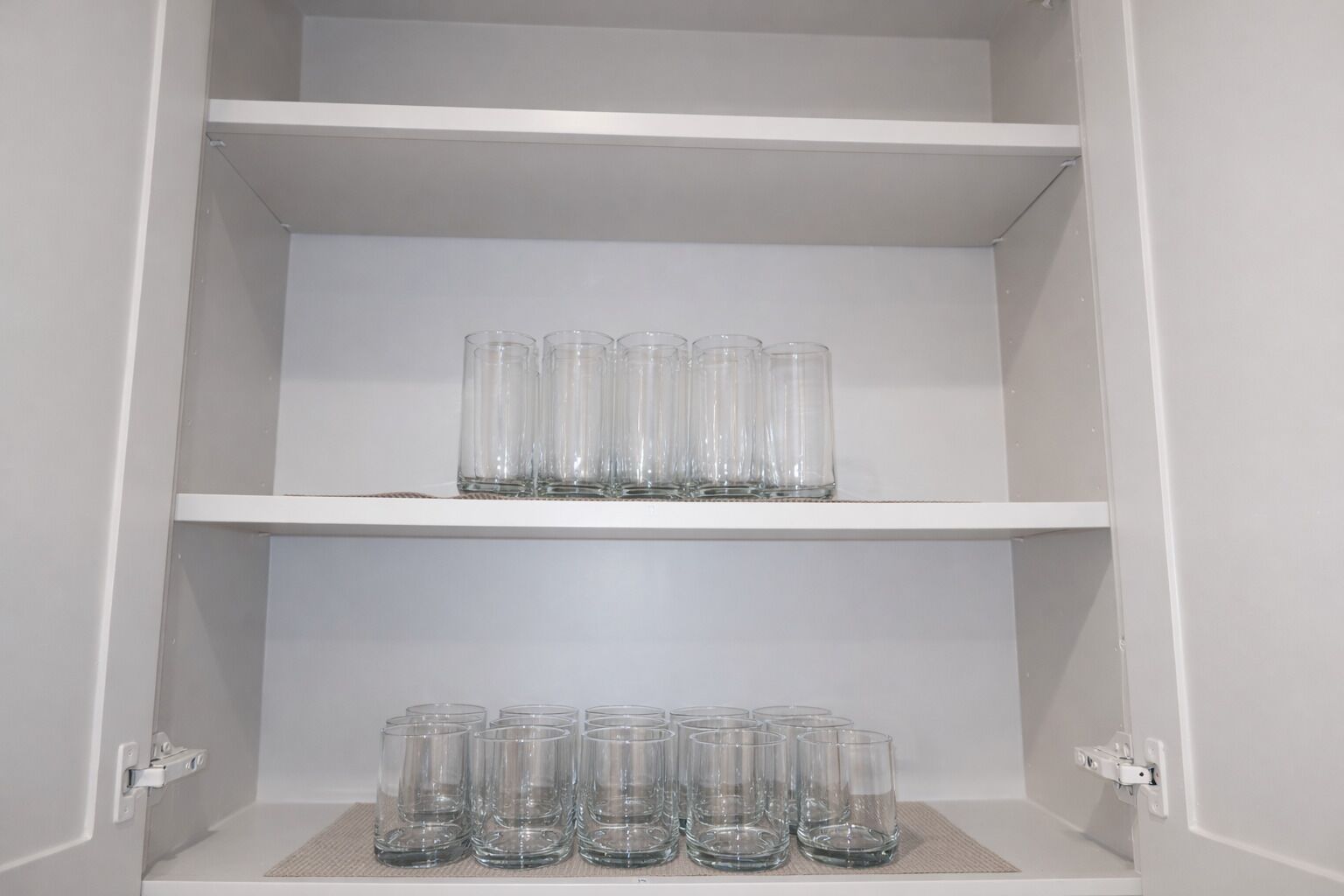 Un mueble blanco con dos estantes, cada uno sosteniendo varios vasos de vidrio transparentes.