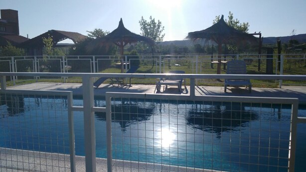 A swimming pool with a tiled deck, sunshade structures, and a fenced area with lounge chairs. - Eluney Cabanas (Mina Clavero)