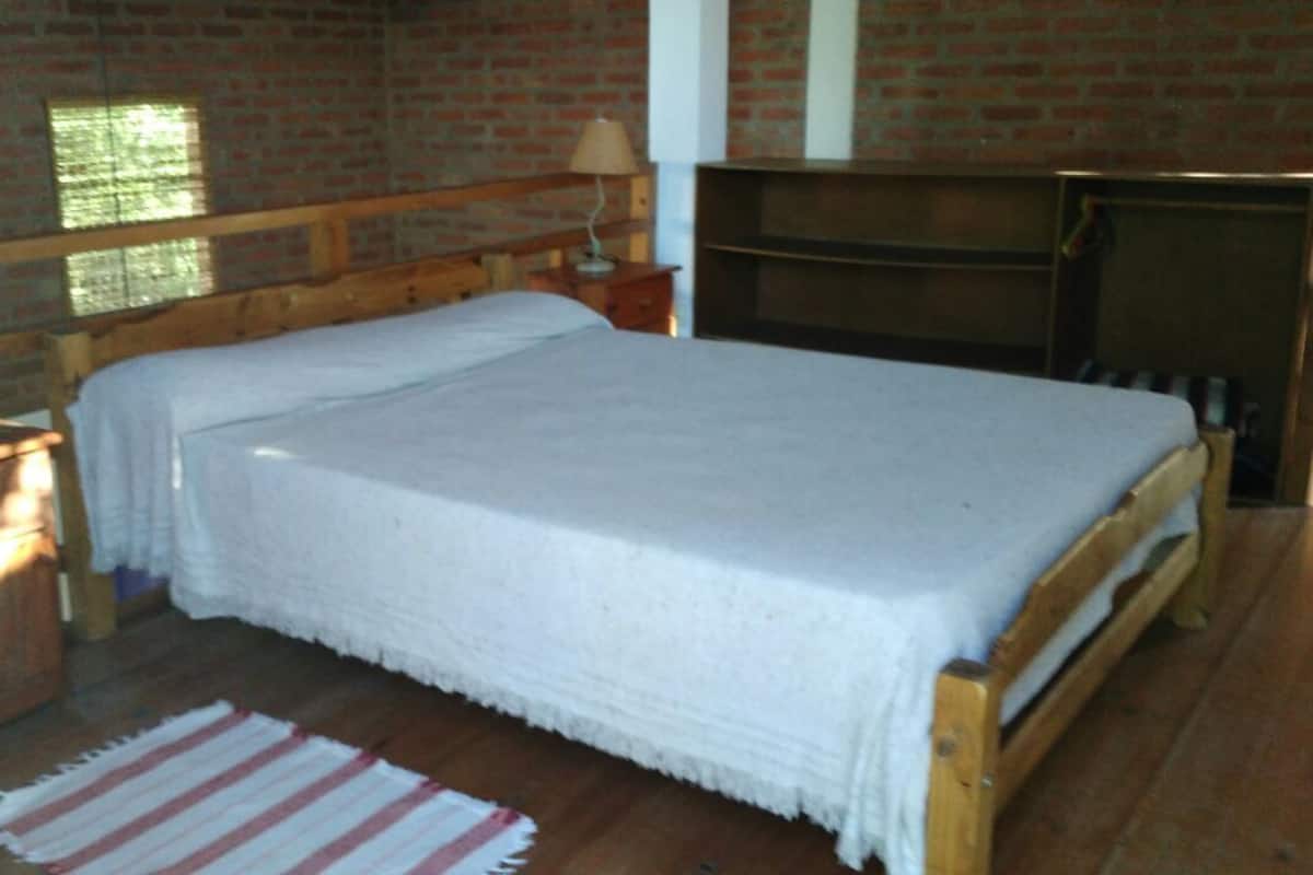 Un dormitorio con cama de madera, mesita de noche, lámpara y pared de ladrillo.