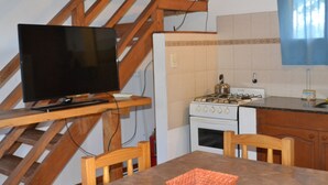 A kitchen with a stove, a television on a wooden stand, and a dining table with chairs. - Eluney Cabanas (Mina Clavero)