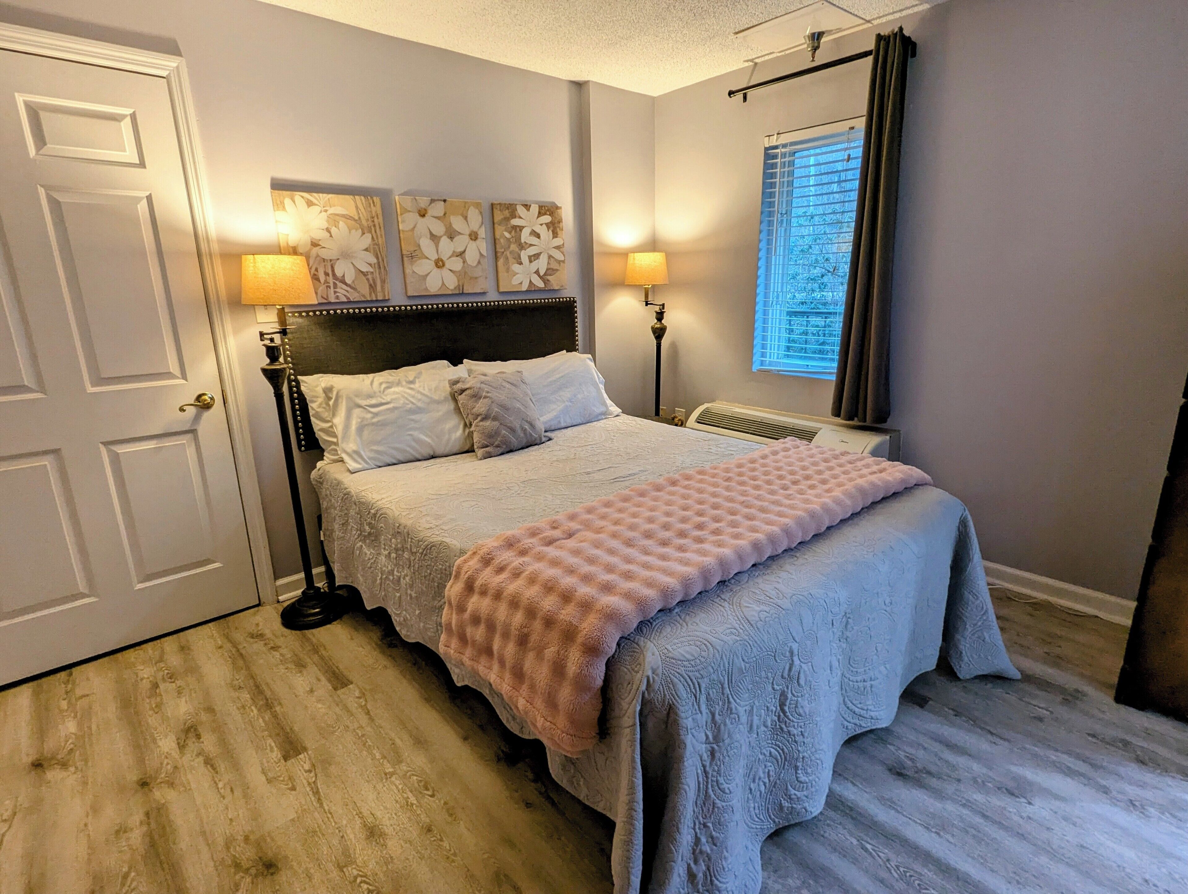 Un dormitorio con cama, lámparas de noche, un radiador y una ventana con persianas.