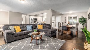 A modern living room with a grey sectional sofa, a round coffee table, and a dining area with a wooden table and chairs.