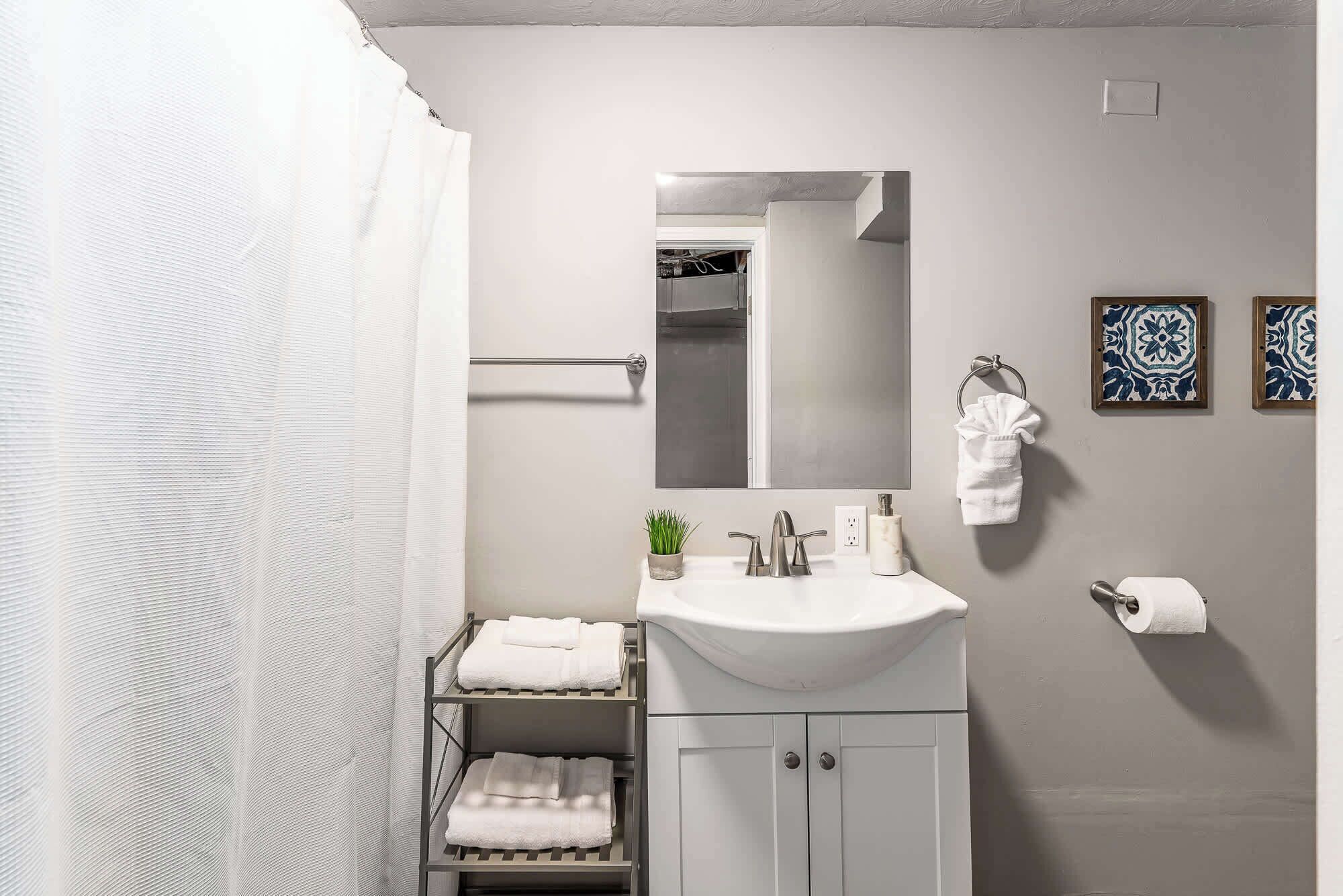 Un baño moderno con un lavamanos blanco, un espejo, un perchero para toallas y una cortina de ducha.