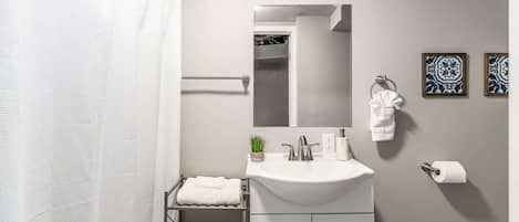Un baño moderno con un lavamanos blanco, un espejo, un perchero para toallas y una cortina de ducha.