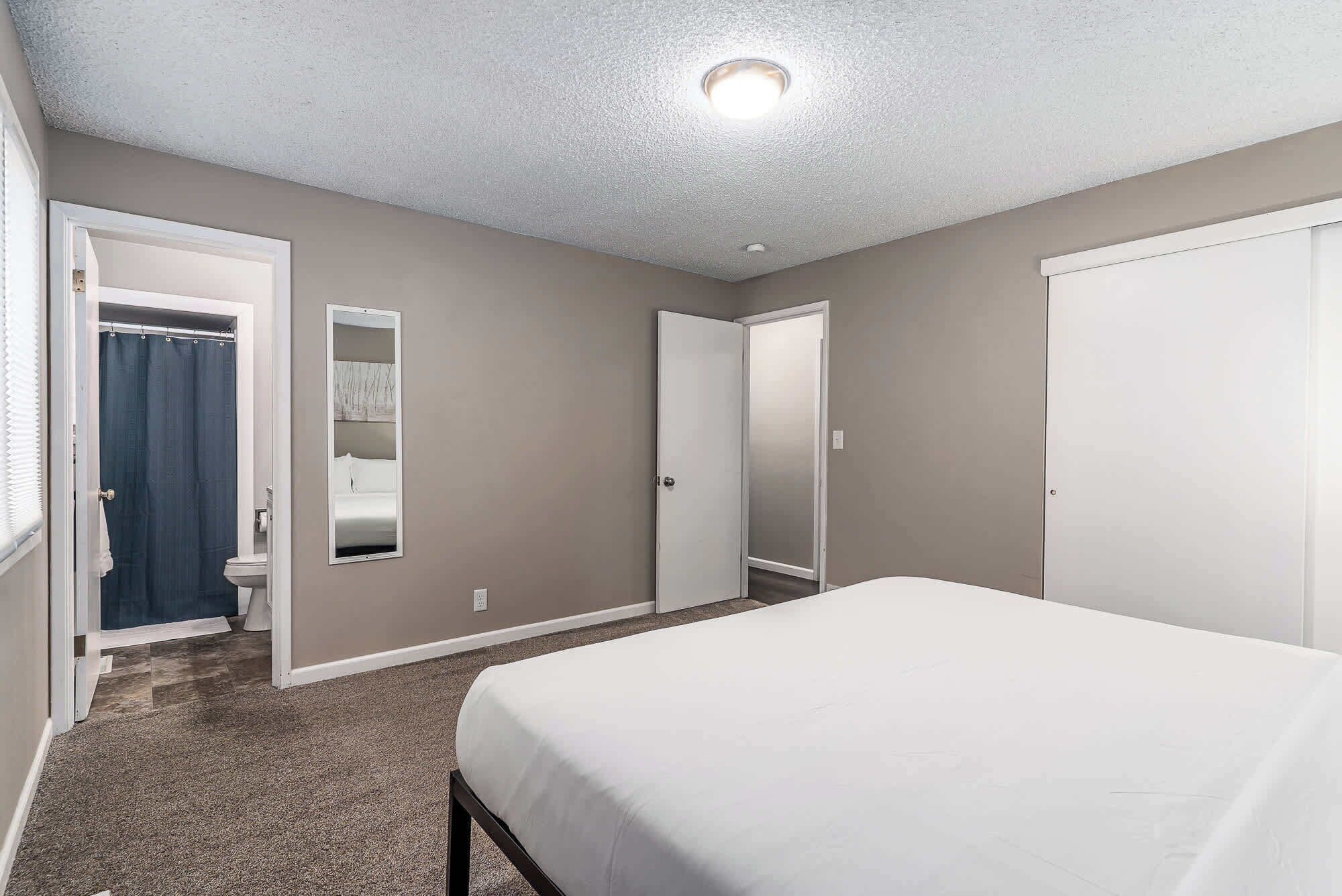 A bedroom with a bed, a bathroom with a shower curtain, and a hallway leading to another room.