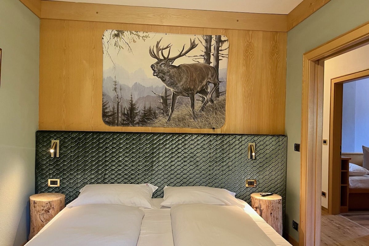 A bedroom with a large bed, wooden headboard, and a wall-mounted deer painting.