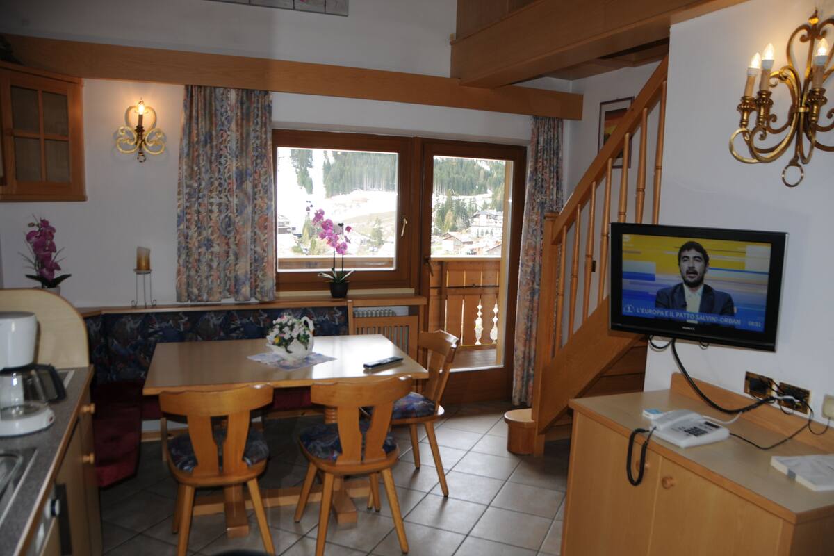 A cozy kitchen with wooden furniture, a dining table, and a TV displaying a news channel.