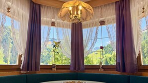 A room with a round table, blue cushioned seating, and large windows with purple curtains. - Wellness Residence Panorama - Check-in at  Olympia Hotel (Livinallongo del Col di Lana)