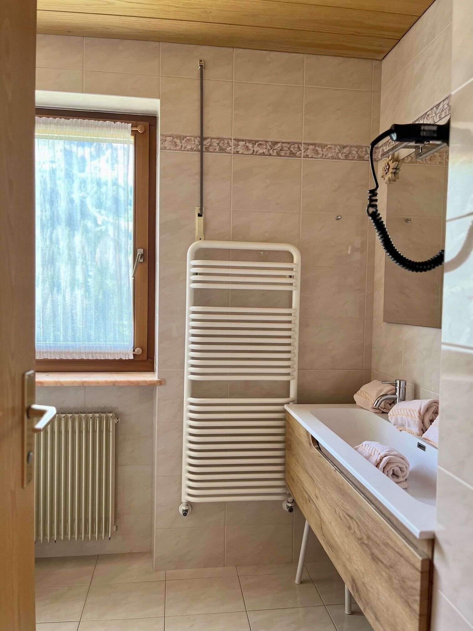 A bathroom with a window, a radiator, a towel rack, and a sink with towels.