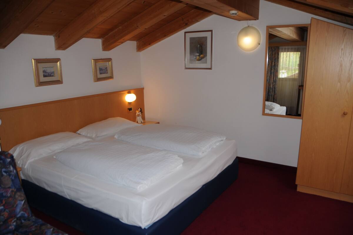 A double bed with white linens in a room with wooden beams on the ceiling.
