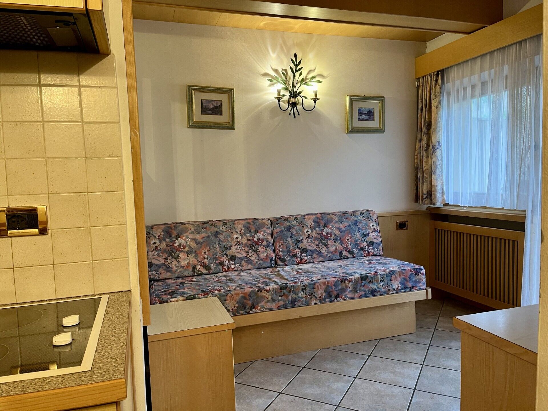 A cozy living area with a floral sofa, a wall-mounted light fixture, and framed pictures.