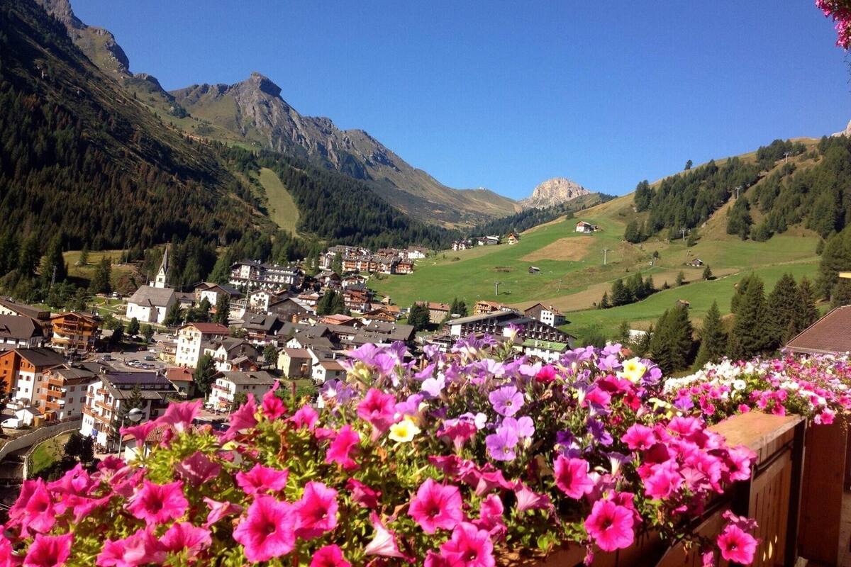 A mountainous town with buildings and a church, surrounded by greenery and mountains.