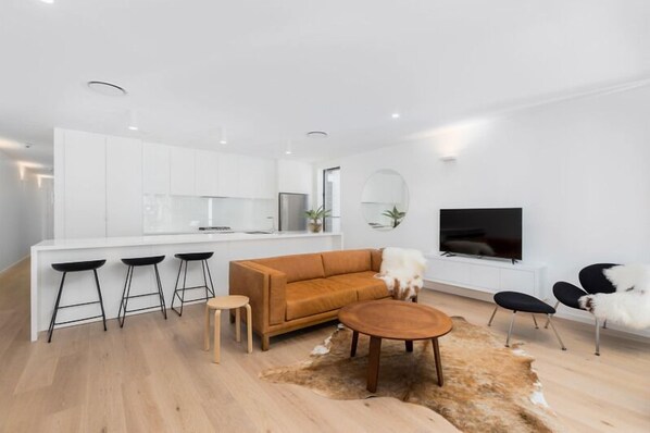 A modern living space with a kitchen, a sofa, a coffee table, and a TV. - 13 First Avenue Sawtell (Sawtell)