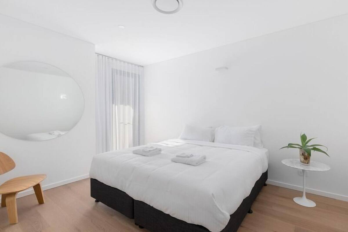 Ein modernes Schlafzimmer mit einem großen Bett, einem runden Spiegel, einem kleinen Tisch mit einer Pflanze und einem Stuhl.