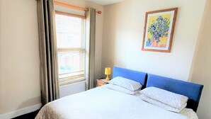 A hotel room with a bed, a nightstand, a lamp, a window with curtains, and a painting on the wall.