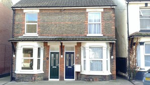 A two-story brick house with a front door, two windows on the ground floor, and a small porch area.